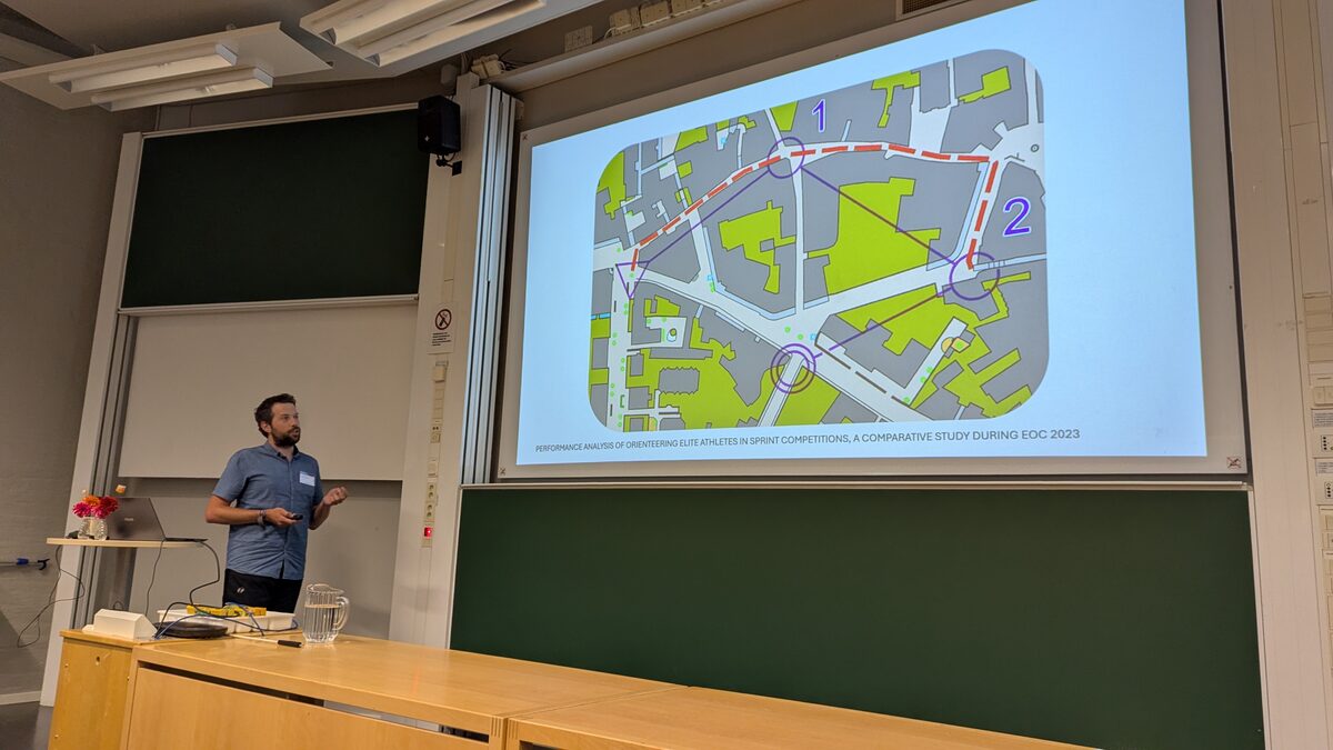 A speaker discussing orienteering routes shown on a projected map